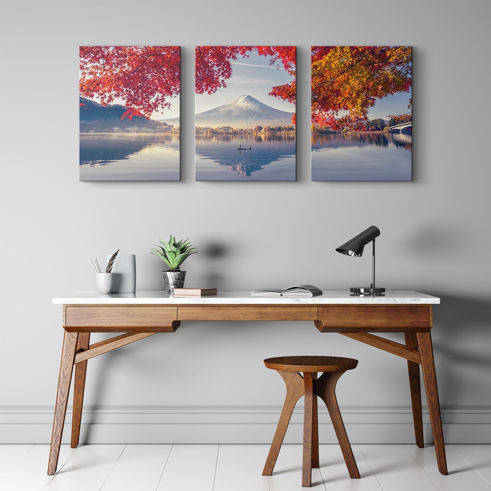 A three-panel canvas of Mount Fuji in autumn above a walnut desk with a black lamp and a round stool.