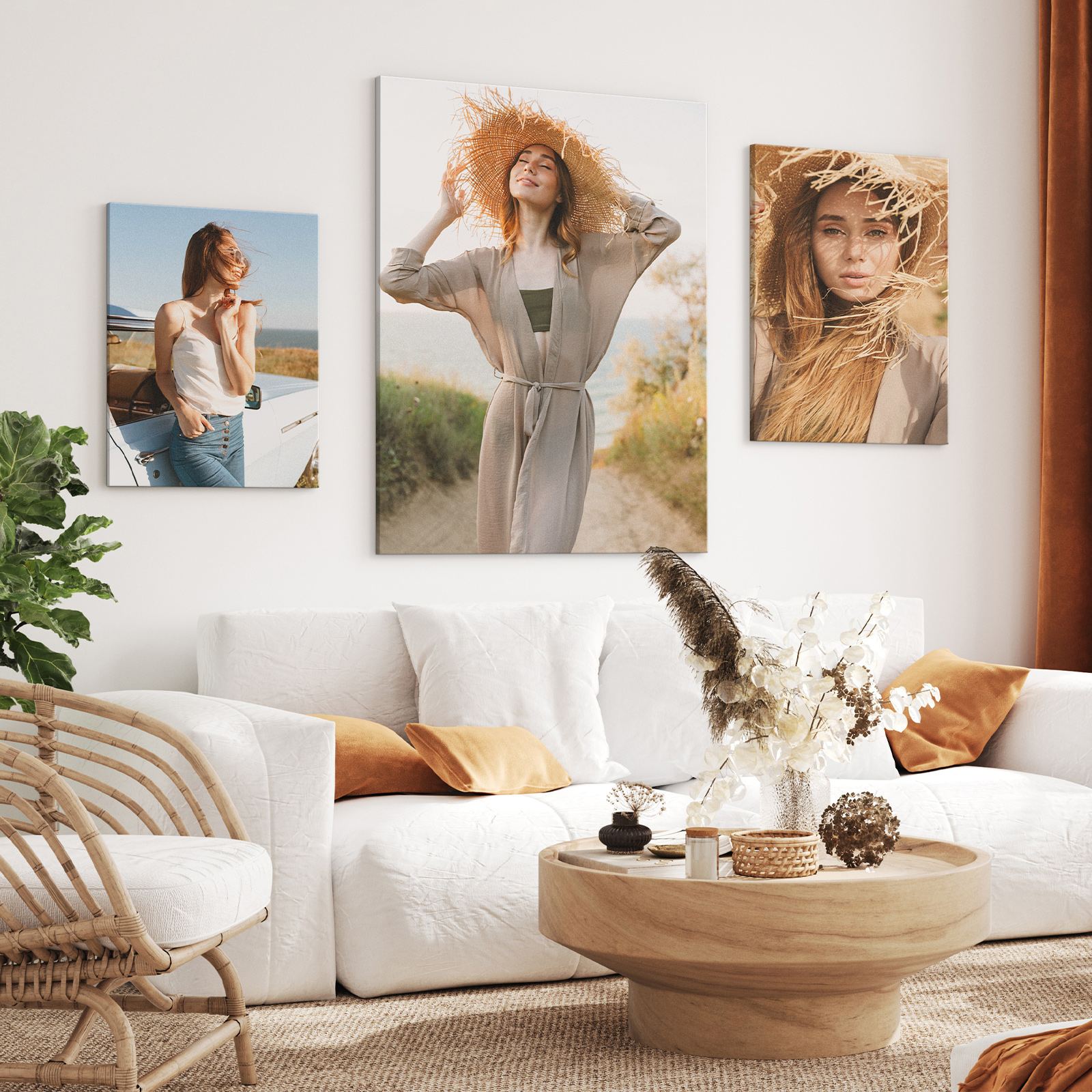 Three canvas portraits of a woman in a straw hat and linen above a white sofa with ochre cushions.
