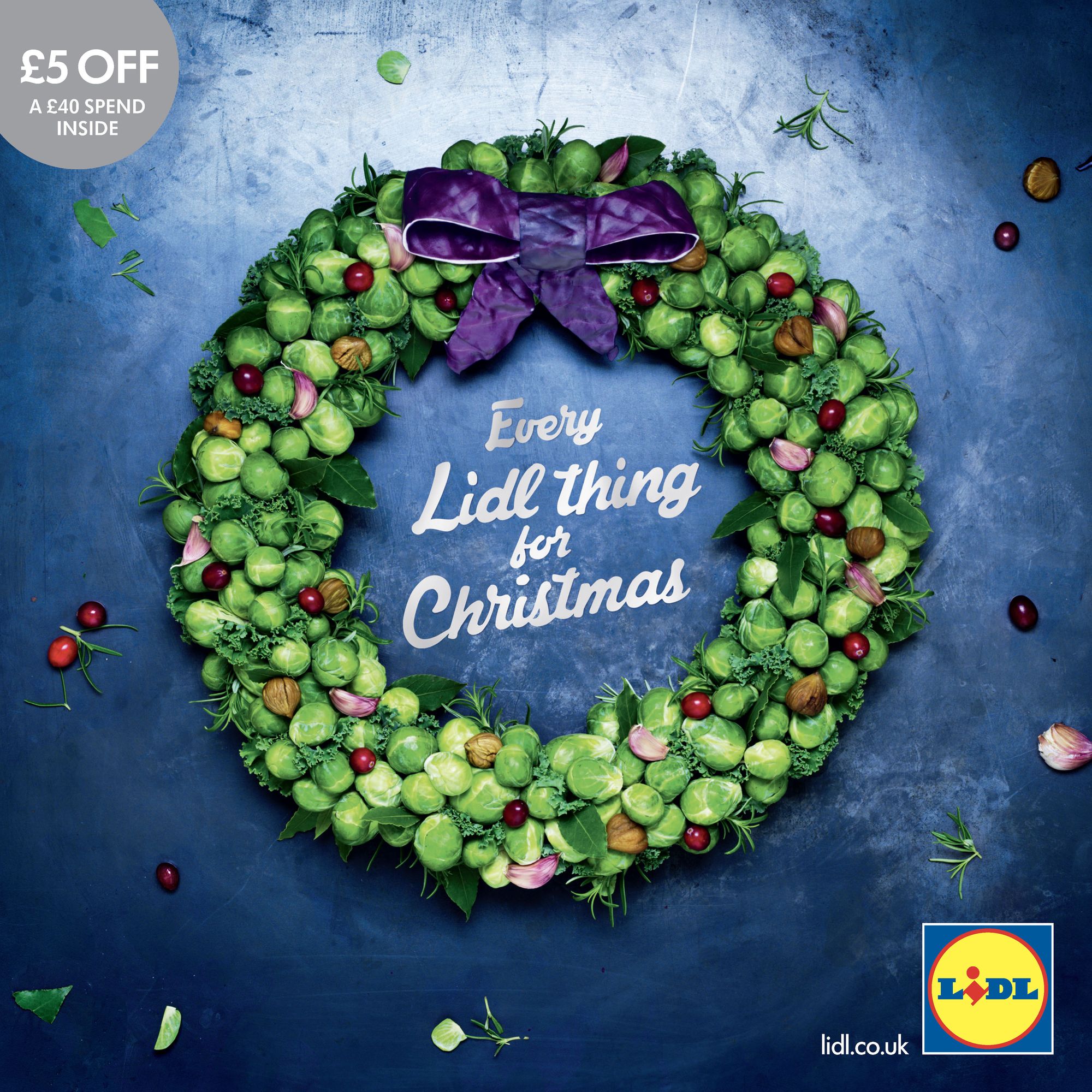 A wreath built from Brussels sprouts, chestnuts, cranberries and bay on a deep blue ground, tied with a purple satin bow.