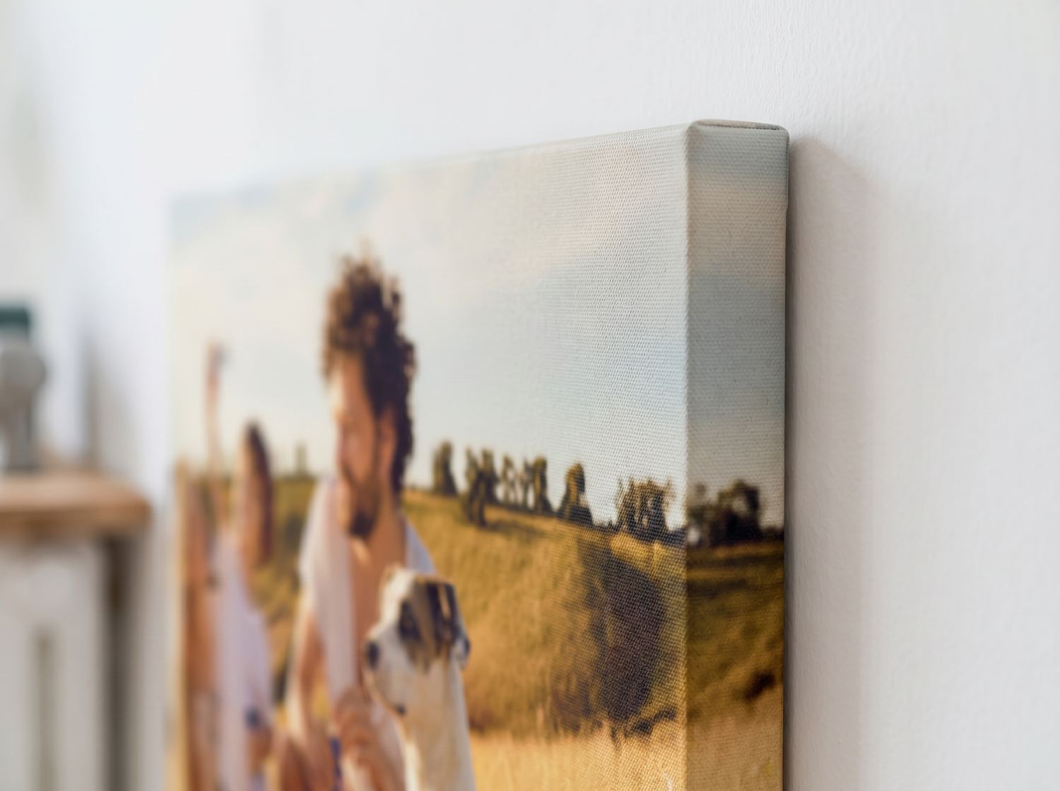 Raking close view of a wrapped canvas corner: the weave at true scale, the photograph continuing over the stretcher edge, and the shadow gap between canvas and wall.