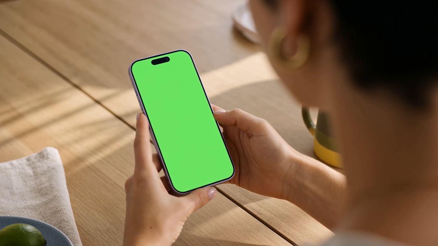 A hand holding a phone whose screen is pure chroma green, generated at the correct perspective and lit by the room, ready for the real interface to be composited in.