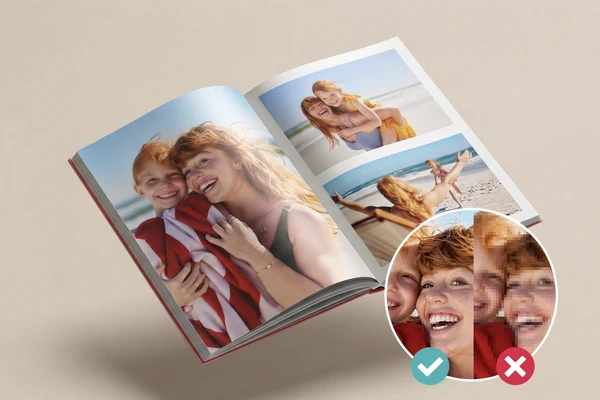 Aufgeschlagenes gedrucktes Fotobuch mit Strandfotos; eine runde Lupe vergleicht denselben Bildausschnitt einmal scharf und einmal verpixelt, markiert mit Haken und Kreuz